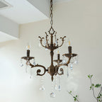 A bronze Clérachic chandelier with three scrolled arms hangs below a white ceiling step, with green twigs behind.