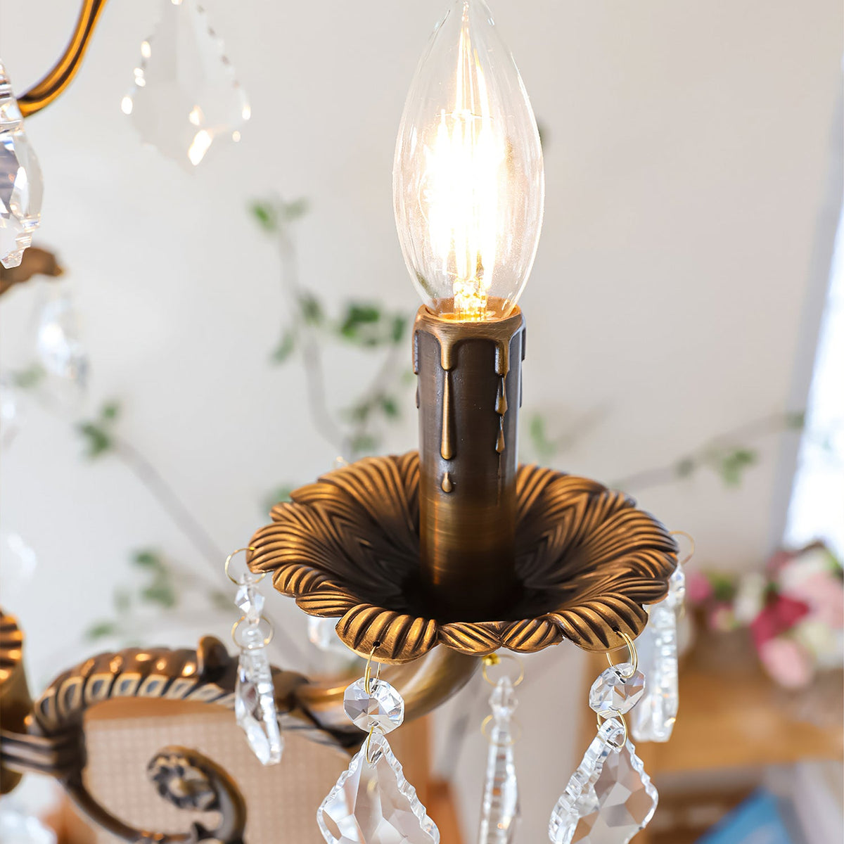 Close view of one candle bulb in a flower-shaped bronze cup on this Clérachic chandelier, with clear prisms beneath.