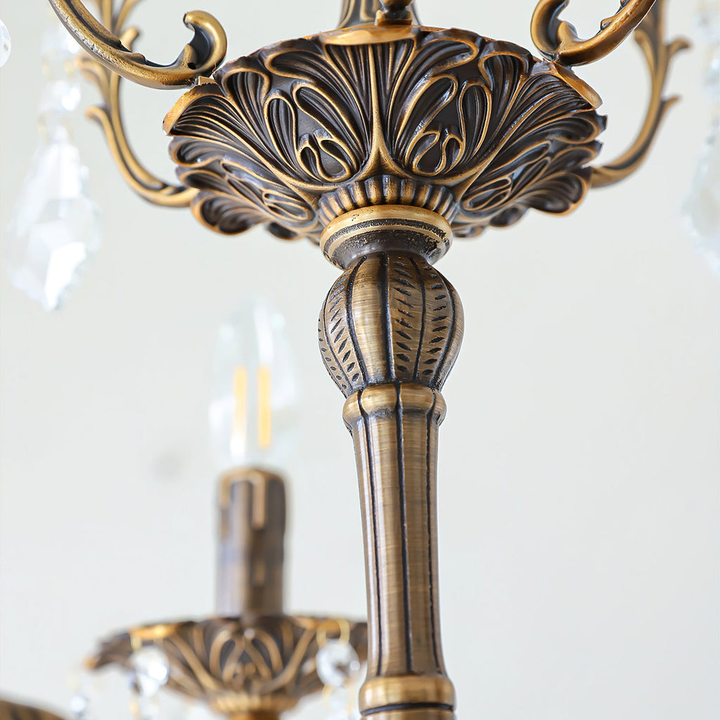 Close view of the carved bronze central column and cup of this Clérachic chandelier, with clear prisms hanging nearby.