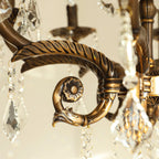 Close view of a leaf-ridged bronze arm ending in a scroll with a rosette on this Clérachic chandelier.