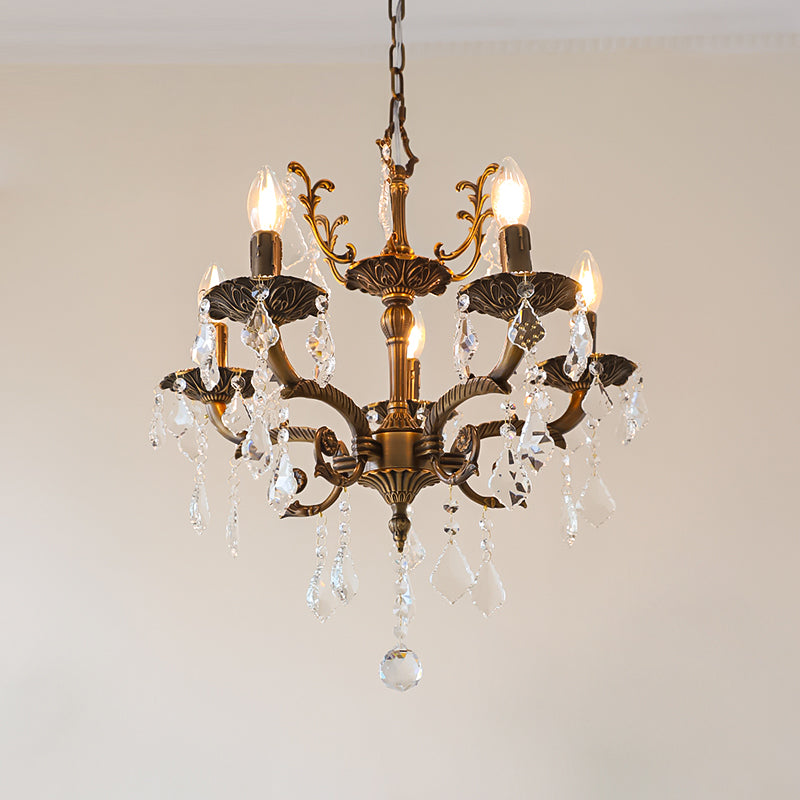 A five-light bronze Clérachic chandelier with clear prisms and a decorative crown hangs against a pale pink wall.