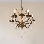 A five-light bronze Clérachic chandelier with clear prisms and a decorative crown hangs against a pale pink wall.