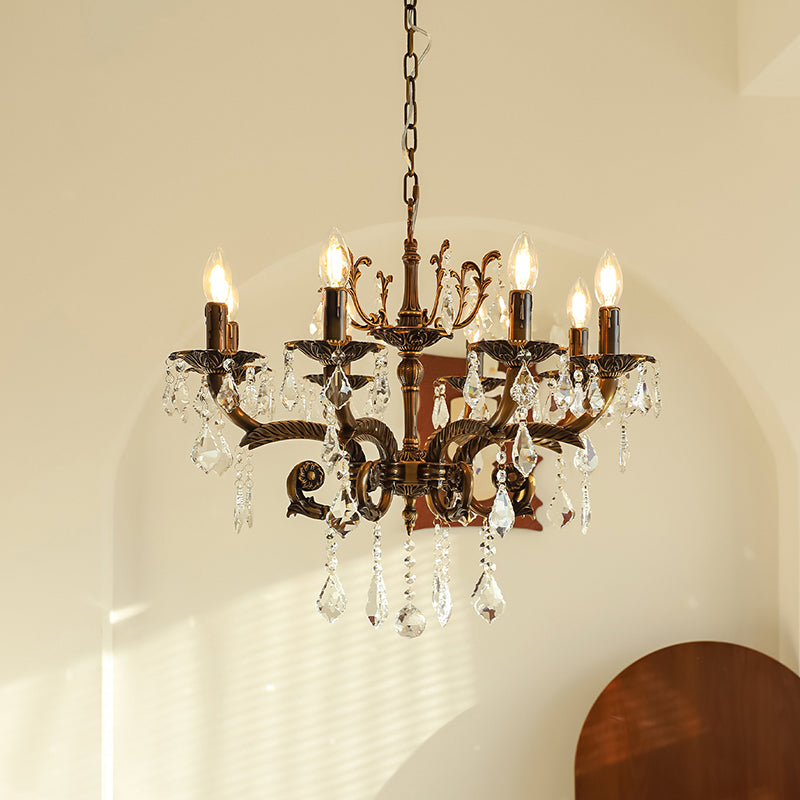 A bronze Clérachic chandelier with eight lit candle bulbs and clear prisms hangs in front of an arched cream wall.