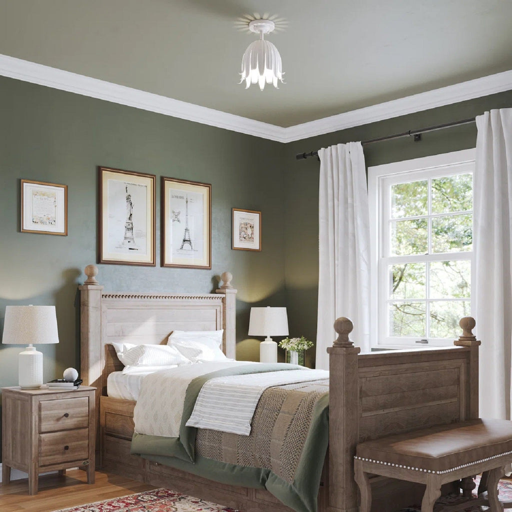 A small white Clérachic petal ceiling light in a green-walled bedroom, with a wooden bed, bedside lamps and framed prints.