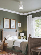 The same green bedroom from further back, with this Clérachic white ceiling light high above the bed and a leather bench at its foot.