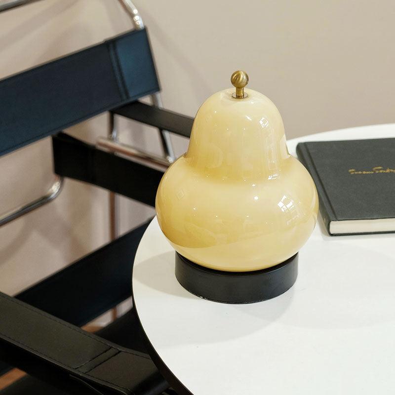 Cream glass Clérachic pear lamp on a small round white table, with a black notebook at its side and a black leather chair behind.