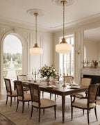 Two Clérachic pendants lit above a long wooden dining table, with an arched window and garden view in a classically panelled room.