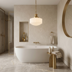 A warmly lit Clérachic pendant hangs in a stone-toned bathroom beside a freestanding white bath and brass fittings.