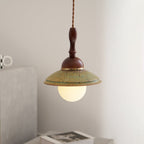 Clérachic pendant hanging close to a grey stone block, its turned wooden stem and brass band above a warm lit globe.