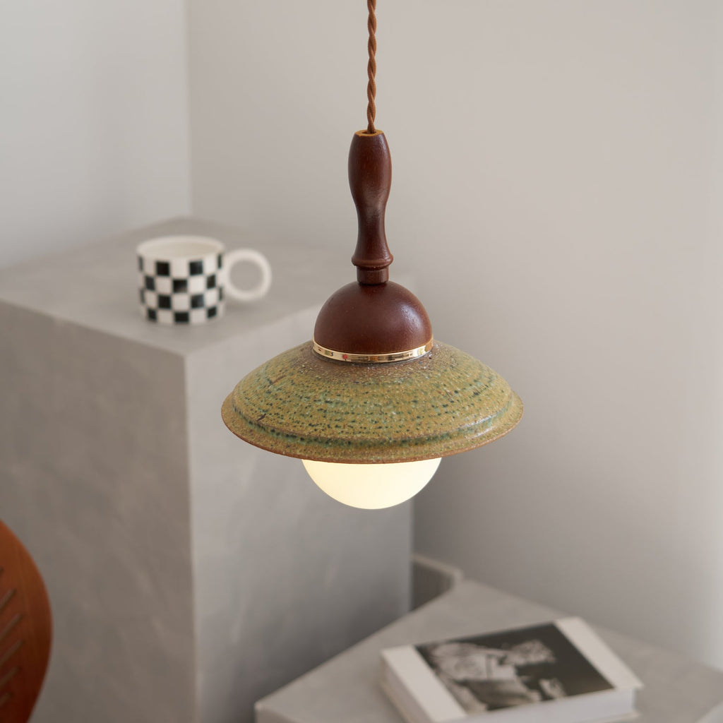 Side-on view of a Clérachic pendant beside a grey plinth with a checkered mug, the green glaze showing fine concentric ridges.