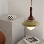 Close framing of this Clérachic pendant's wide green ceramic shade and walnut-coloured dome, with grey blocks and a book behind.