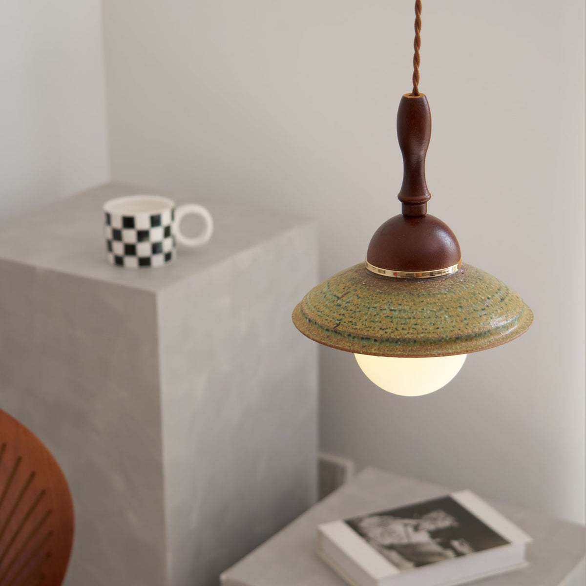 Close framing of this Clérachic pendant's wide green ceramic shade and walnut-coloured dome, with grey blocks and a book behind.
