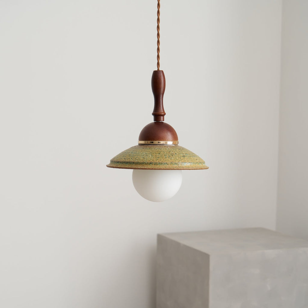 Unlit Clérachic pendant with a white globe under a green ceramic shade, against a plain pale wall with a grey block below.