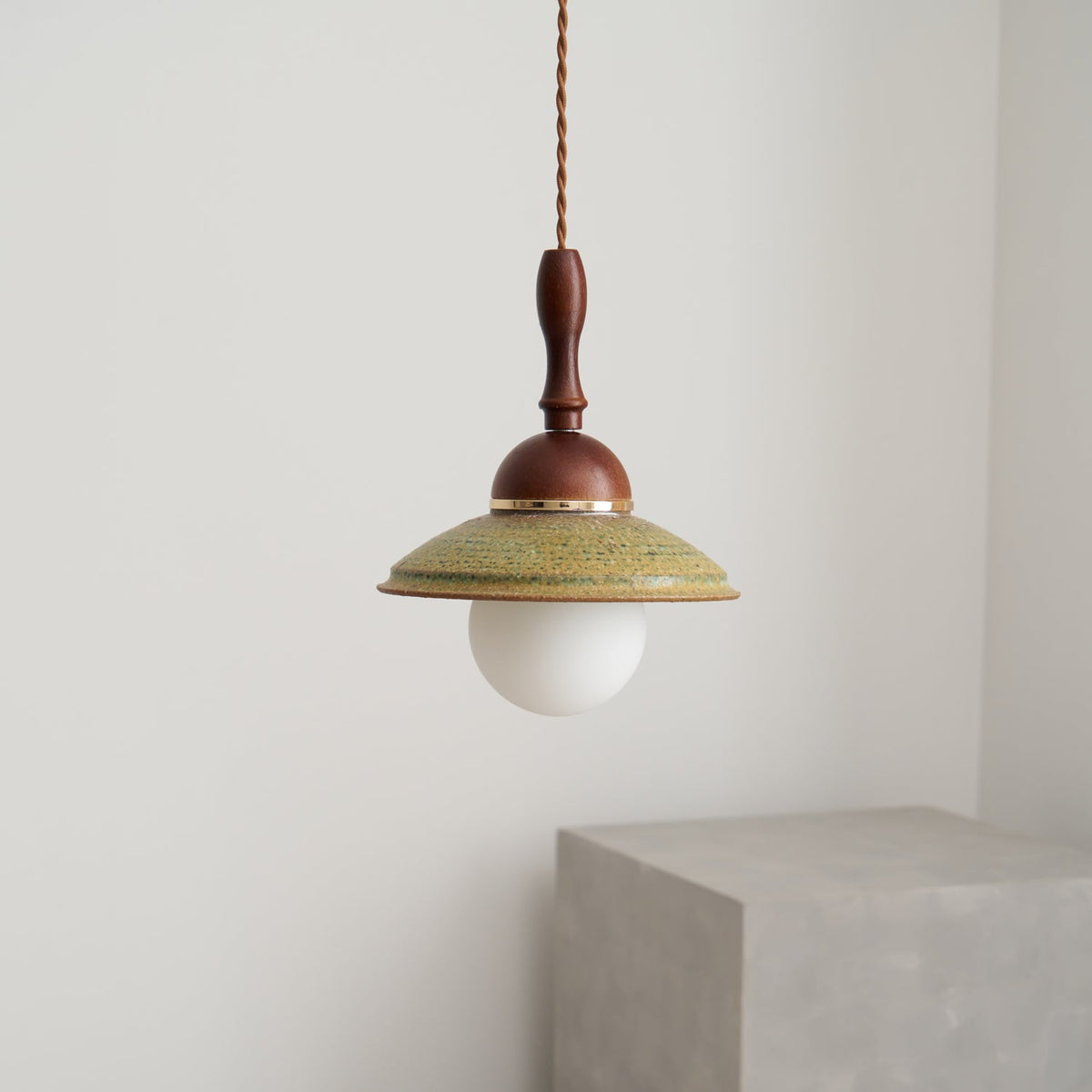 Unlit Clérachic pendant with a white globe under a green ceramic shade, against a plain pale wall with a grey block below.