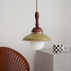 Clérachic pendant with an unlit white globe, a green stoneware shade and brass trim, near a checkered mug and a wooden chair.