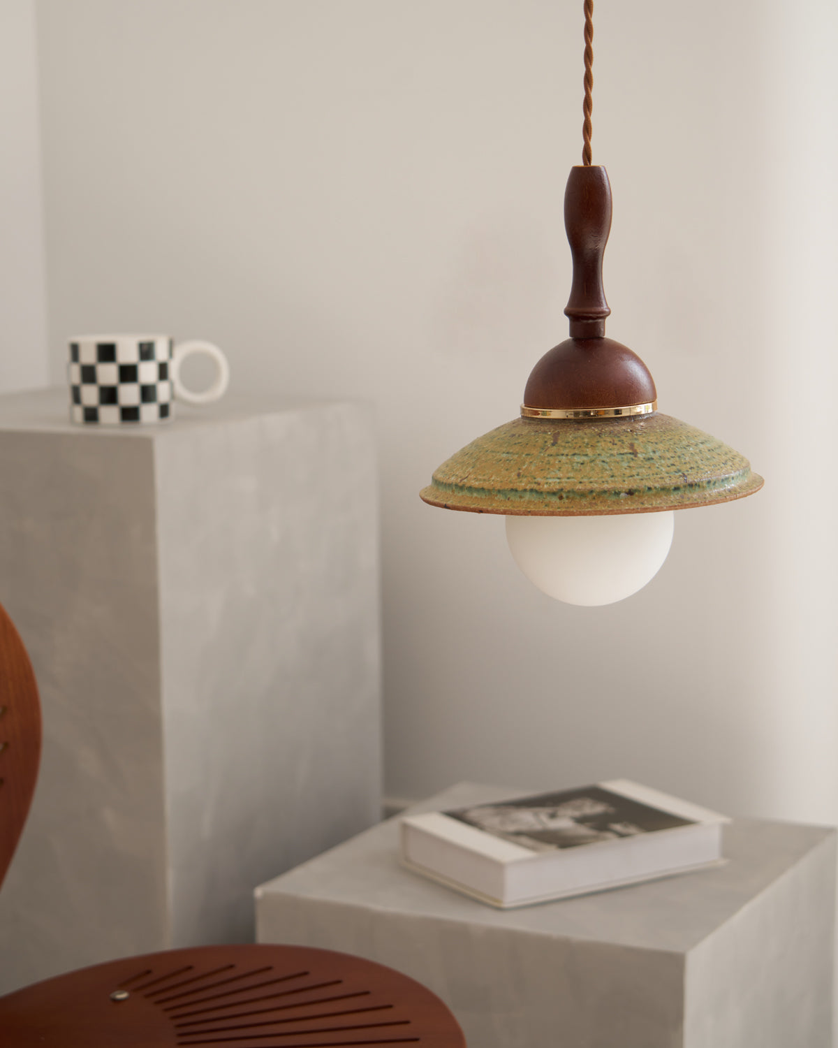 Unlit Clérachic pendant with a white globe under its green shade, above grey stone blocks holding a mug and a book.