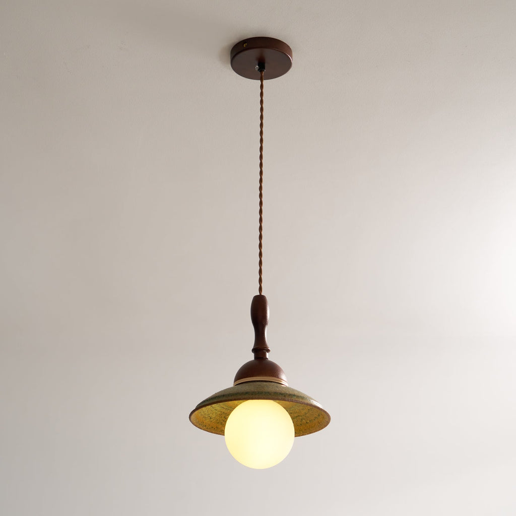 Clérachic pendant on its long twisted cord from a round walnut-coloured ceiling canopy, with the globe lit below the green shade.