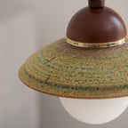 Close view of the speckled green glaze, brass band and walnut-coloured dome on this Clérachic pendant shade.