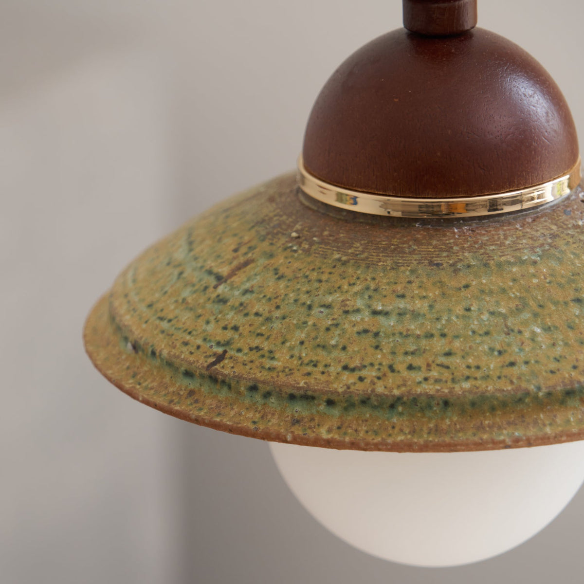 Close view of the speckled green glaze, brass band and walnut-coloured dome on this Clérachic pendant shade.
