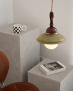 Clérachic pendant with a softly lit globe above a grey block with a checkered mug, a book and a chair back below.