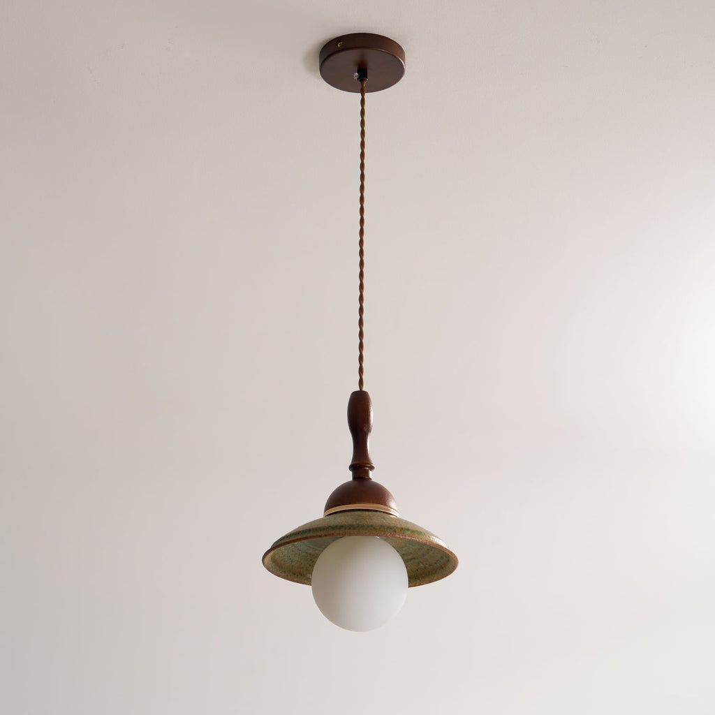 Unlit Clérachic pendant hanging from its round walnut-coloured canopy on a twisted cord, against a plain pale ceiling and wall.