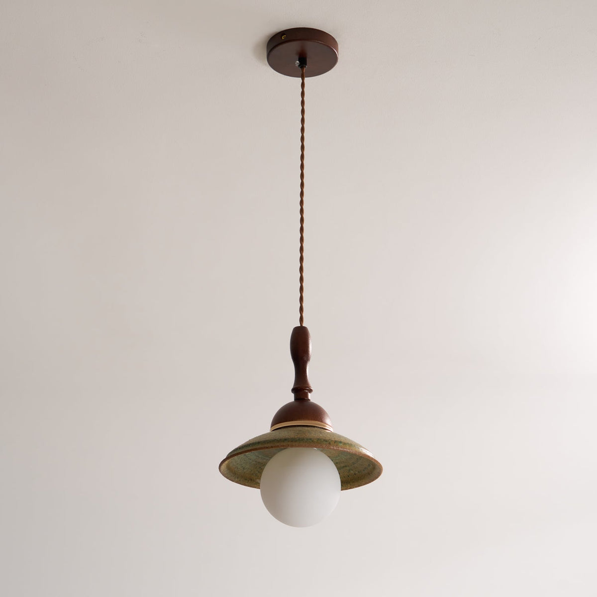 Unlit Clérachic pendant hanging from its round walnut-coloured canopy on a twisted cord, against a plain pale ceiling and wall.