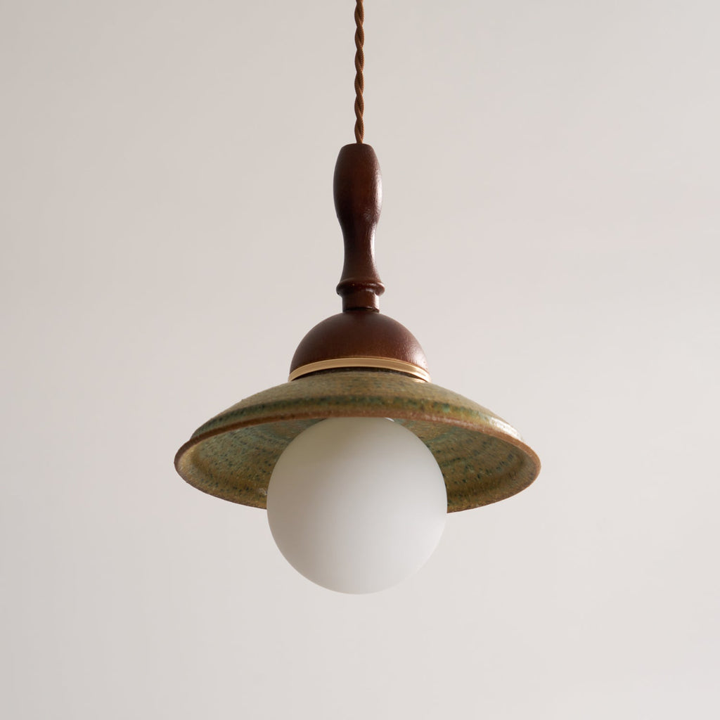 Front view of an unlit Clérachic pendant, the wide green ceramic shade sitting over a round white globe.