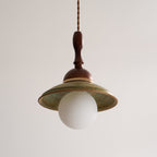 Front view of an unlit Clérachic pendant, the wide green ceramic shade sitting over a round white globe.