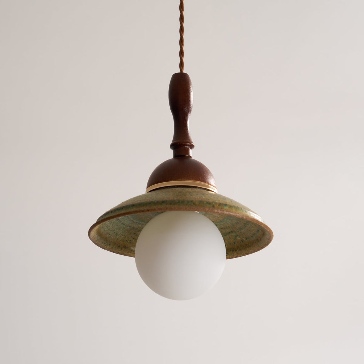 Front view of an unlit Clérachic pendant, the wide green ceramic shade sitting over a round white globe.
