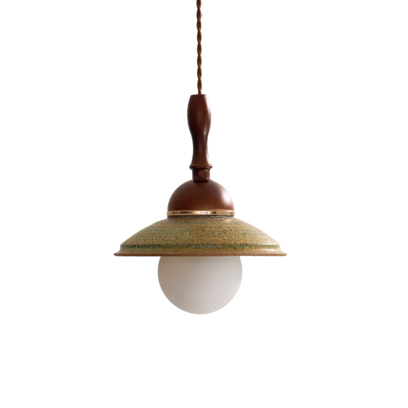 Clérachic pendant on a plain white backdrop, with a turned wooden stem, a brass band, a green ceramic shade and a white globe.