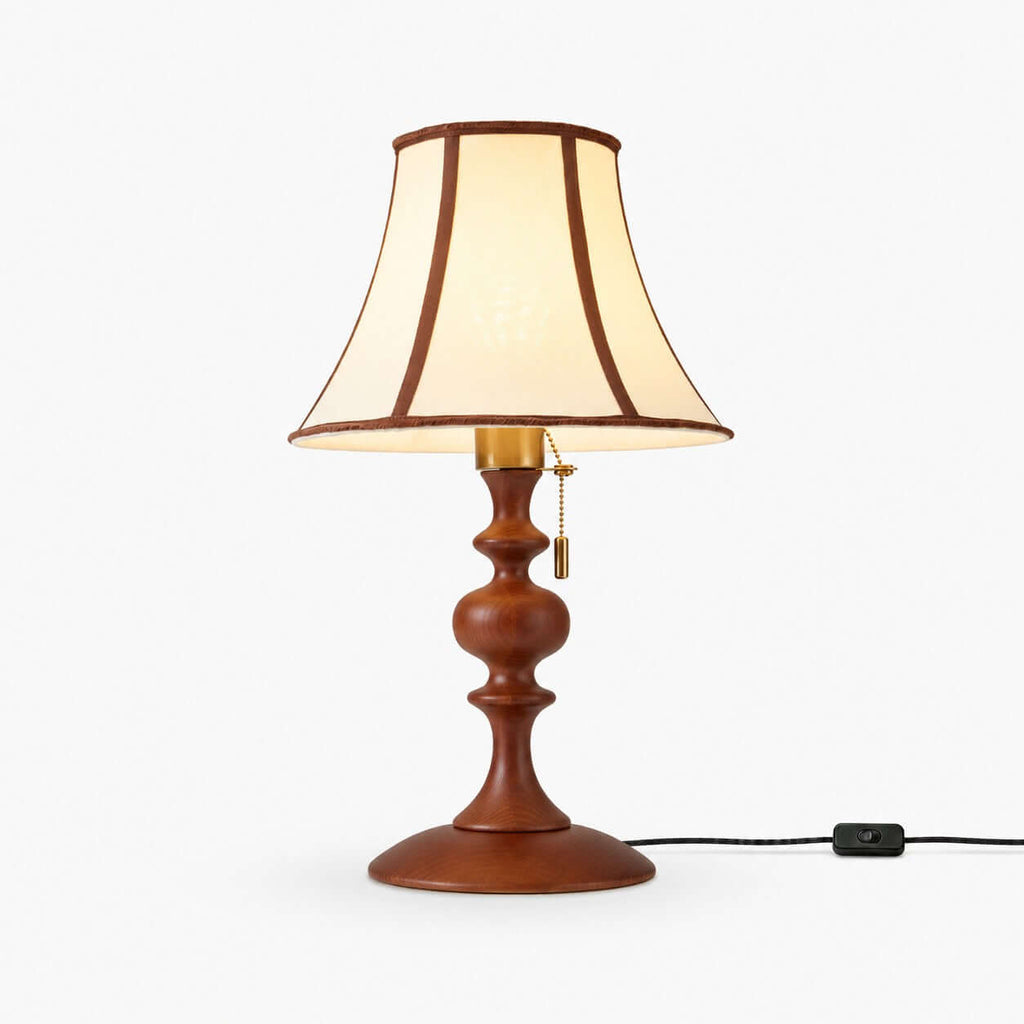 This Clérachic table lamp on a white backdrop, a flared off-white shade with dark brown piping over a turned walnut-toned wood base and a pull chain.