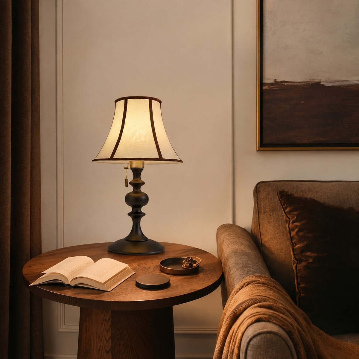 Clérachic lamp with a black base on a round wooden side table, beside an open book and a brown armchair with a rust throw.