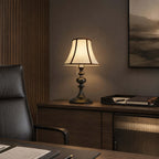 A Clérachic lamp with a black base on a dark wooden sideboard, with a leather desk chair and a dark landscape print behind.