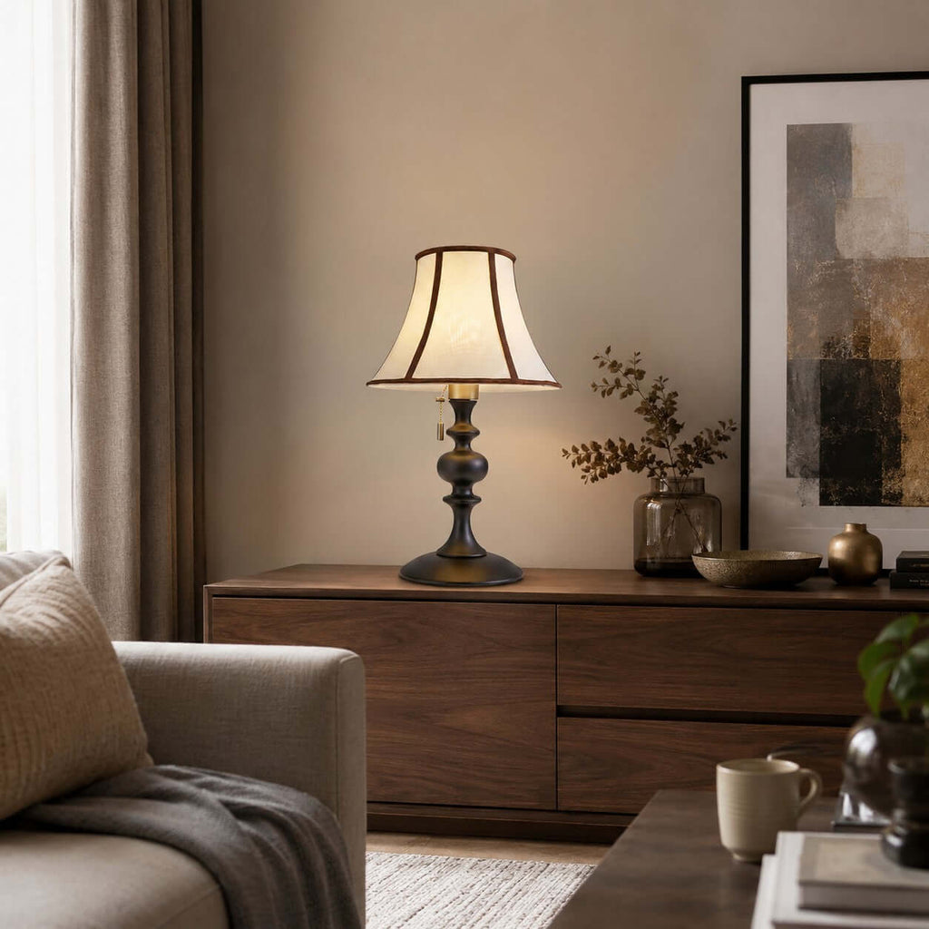 Clérachic table lamp in black and beige on a walnut sideboard, next to a glass vase of dried branches and a pale sofa.