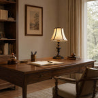 Distant view of the black-base Clérachic lamp on a wooden desk, with a pen pot, an open notebook and framed art on the wall.