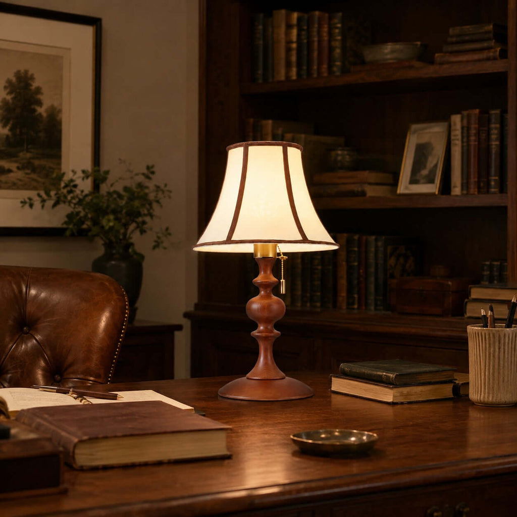 The Clérachic lamp in walnut on a dark desk, among old books, a brass dish and a leather chair, in front of a bookcase.