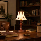 The Clérachic lamp in walnut on a dark desk, among old books, a brass dish and a leather chair, in front of a bookcase.