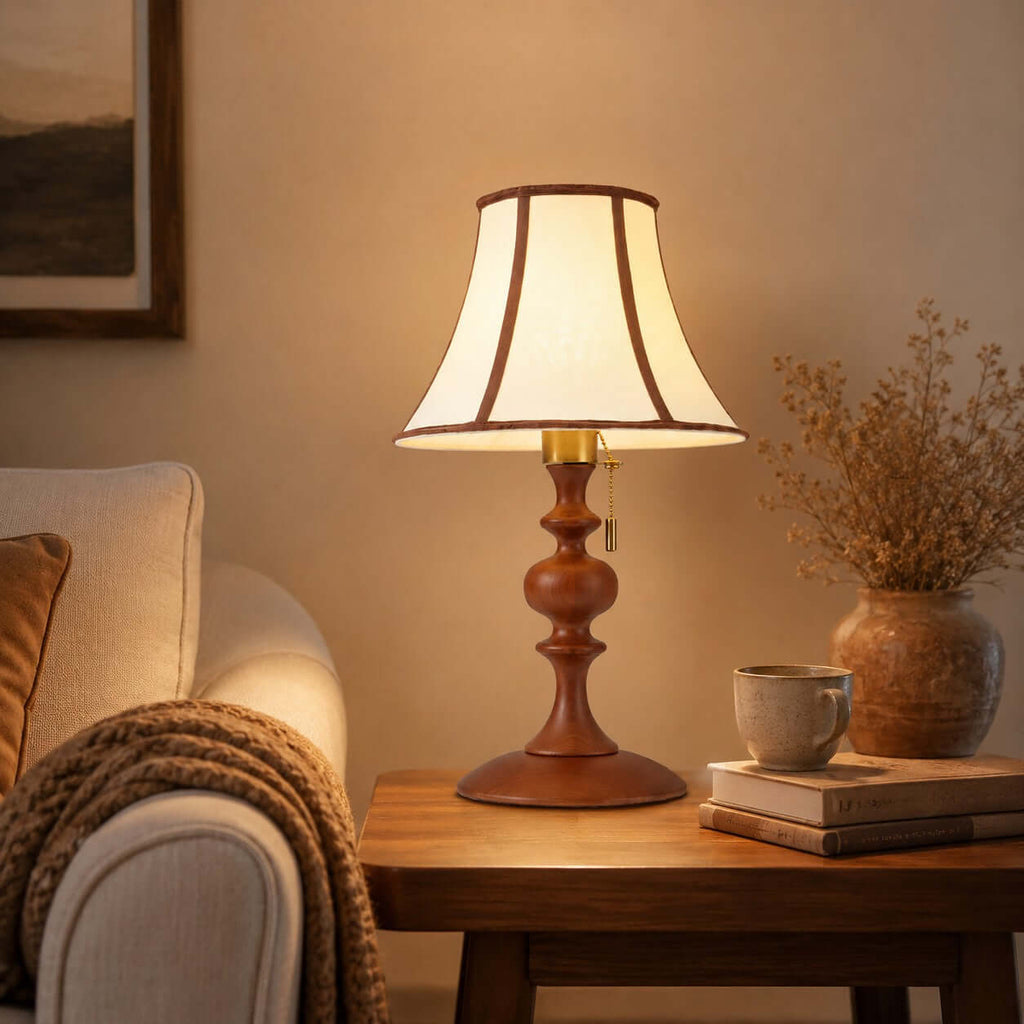 Close view of the lit walnut Clérachic lamp on a side table beside a cream sofa, with a stone mug, books and dried stems.