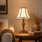 Close view of the lit walnut Clérachic lamp on a side table beside a cream sofa, with a stone mug, books and dried stems.