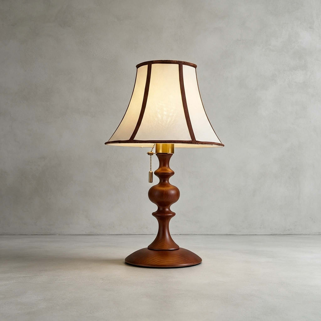 Walnut Clérachic table lamp on a plain grey concrete floor and wall, with a pull chain hanging from the brass socket.
