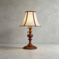 Walnut Clérachic table lamp on a plain grey concrete floor and wall, with a pull chain hanging from the brass socket.