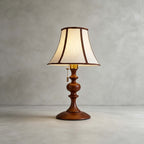Walnut Clérachic table lamp on a plain grey concrete floor and wall, with a pull chain hanging from the brass socket.