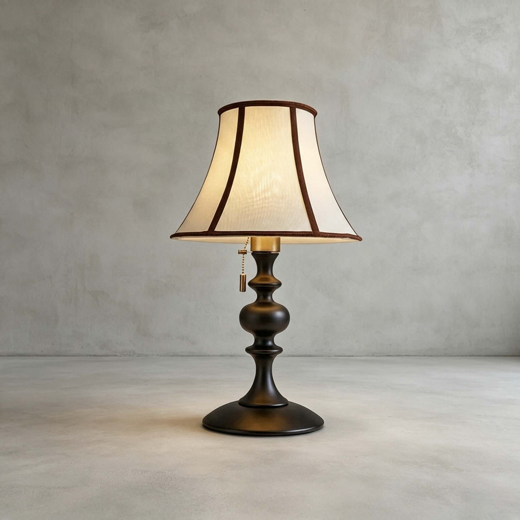 Black-base Clérachic table lamp on a plain grey concrete floor and wall, its flared shade lit warm.