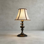 Black-base Clérachic table lamp on a plain grey concrete floor and wall, its flared shade lit warm.