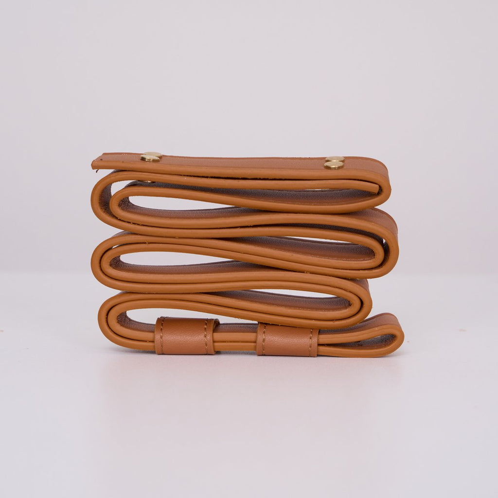 Clérachic Vista's tan faux-leather hanger coiled on white, its brass rivets and stitched edges in close view.