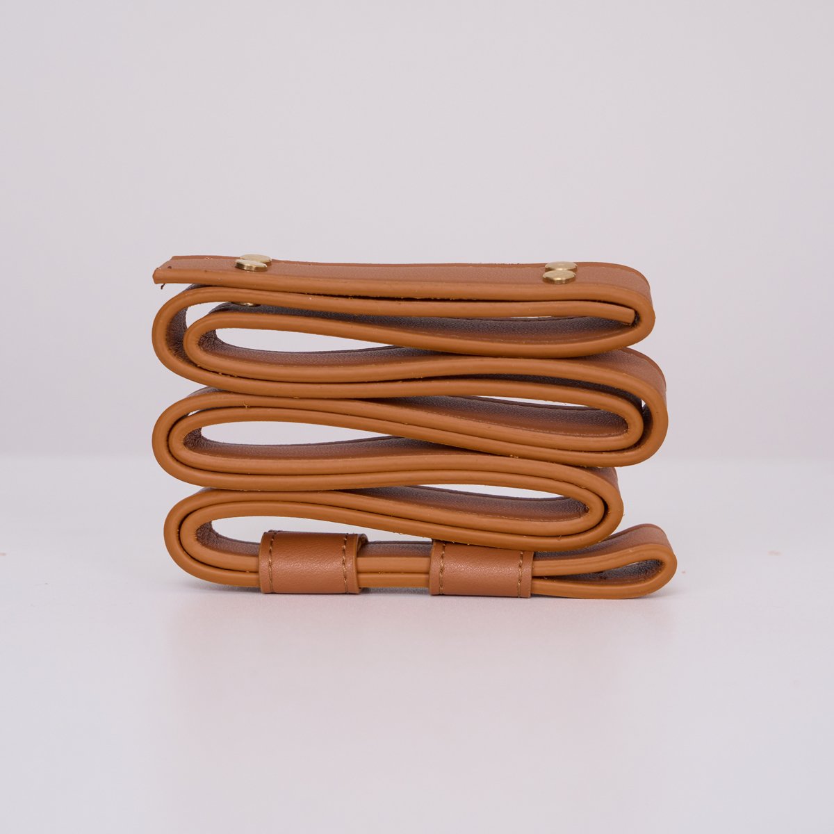 Clérachic Vista's tan faux-leather hanger coiled on white, its brass rivets and stitched edges in close view.