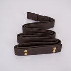 Clérachic Vista's dark brown faux-leather strap coiled flat, brass rivet heads set into the folded end.