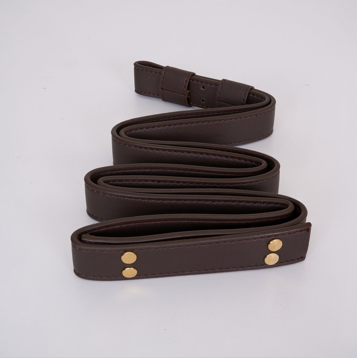 Clérachic Vista's dark brown faux-leather strap coiled flat, brass rivet heads set into the folded end.