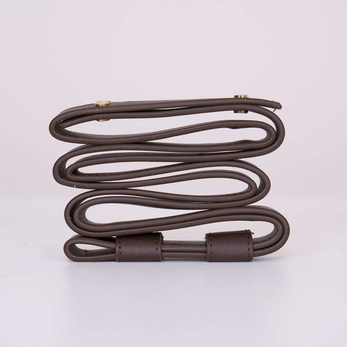 Clérachic Vista strapping in dark brown, looped and clasped with brass fittings on a plain white surface.