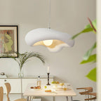 White Clérachic wavy-edged pendant above a dining table set with fruit and a candlestick, beside a framed print and a palm.